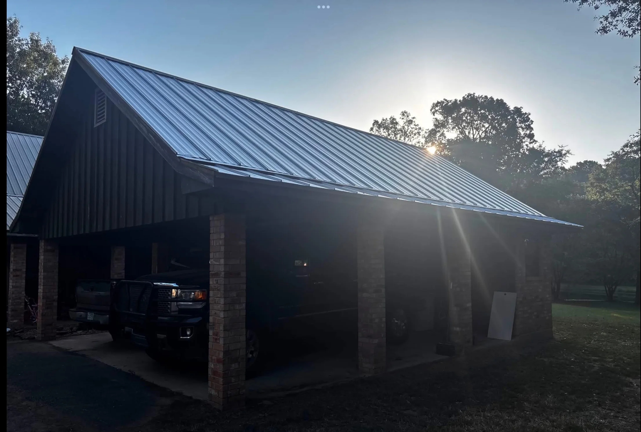 Dark gray standing seam metal roof on agricultural building with brick columns and concrete pad