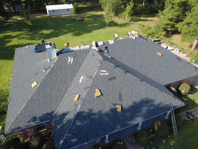 Aerial view of residential roof with gray architectural shingles, multiple planes, and installation crew at work