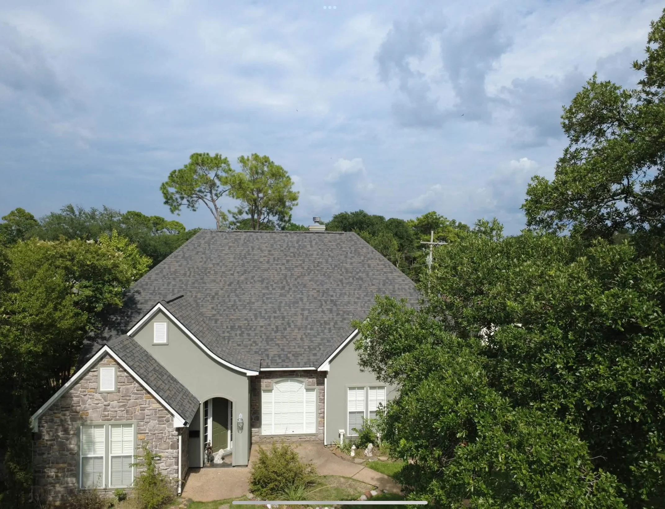 Charcoal gray asphalt shingle roof on curved multi-pitched residential home with stone and stucco exterior